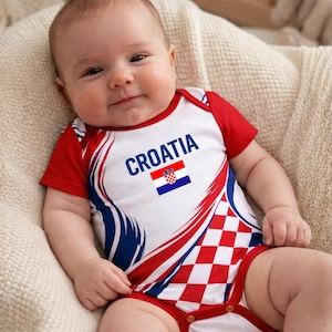May include: A baby wearing a red, white, and blue bodysuit with the word "CROATIA" and the Croatian flag. The bodysuit has a checkered pattern on the bottom and a design that resembles a flag.