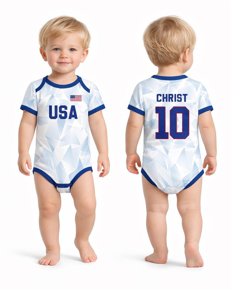 Puede incluir: Body de beb&eacute; blanco con un patr&oacute;n geom&eacute;trico y ribetes azules. La parte delantera presenta el texto "USA" y una peque&ntilde;a bandera estadounidense. La parte trasera muestra "CHRIST" y el n&uacute;mero "10" en azul.