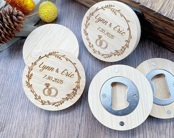 May include: Bamboo bottle opener favors with engraved text "Lynn & Eric 7.30.2025" and a ring design. The round openers have a silver metal opener on the bottom. Wedding favors.
