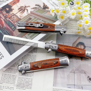 May include: Three folding knives with wooden handles and silver accents are displayed. One knife has a comb blade, and another has the word "Tom" etched on the handle. The knives are on a newspaper with white flowers in the background.