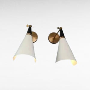May include: Two mid-century modern wall sconces. Each sconce features a white, cone-shaped shade, a black top, and a brass-colored mounting plate. The sconces are designed to be mounted on a wall and provide directional lighting.