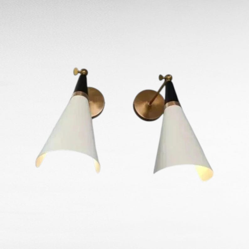 May include: Two mid-century modern wall sconces. Each sconce features a white, cone-shaped shade, a black top, and a brass-colored mounting plate. The sconces are designed to be mounted on a wall and provide directional lighting.