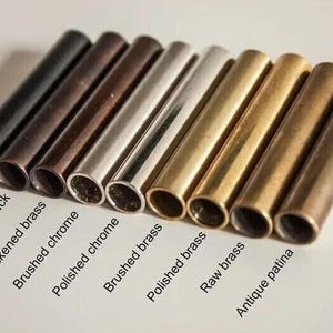 May include: An assortment of metal tubes in various finishes, including matte black, antique black, and polished brass. The tubes are arranged diagonally, showcasing a range of colors and textures. Text labels identify each finish, offering a visual guide to the different options.