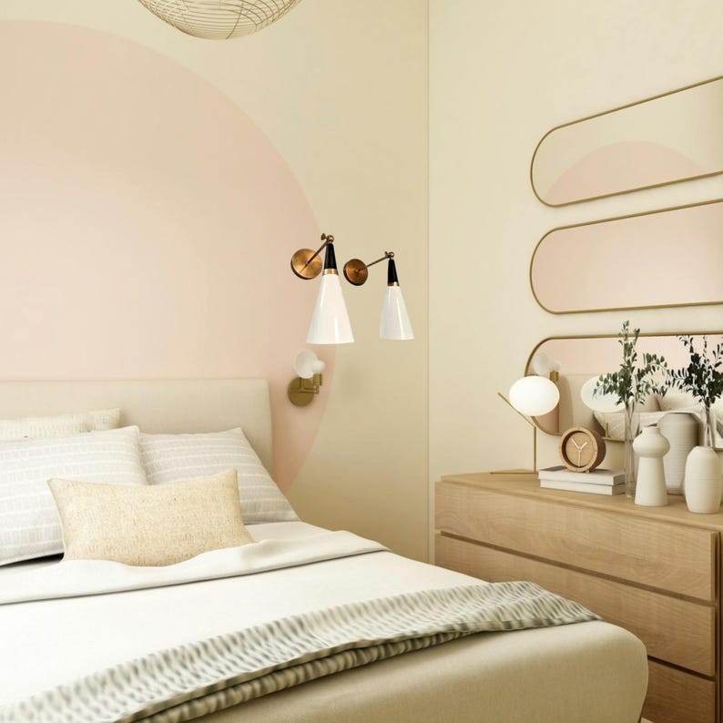 May include: A bedroom scene with a bed, dresser, and wall decor. The bed has white bedding and a light-colored headboard. Two white cone-shaped lamps are mounted on the wall. A dresser with a mirror and decorative items is on the right.
