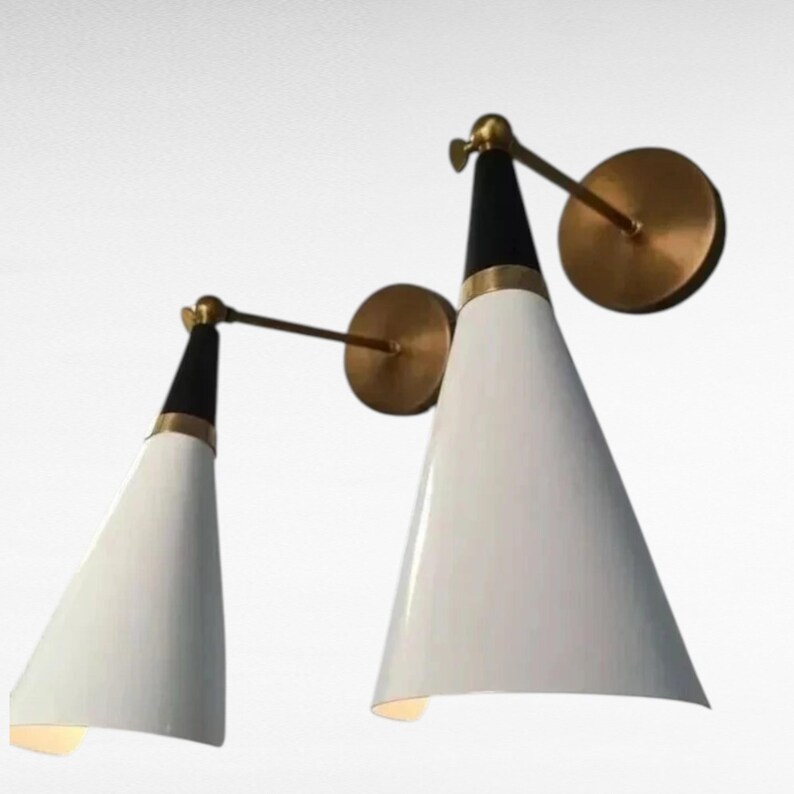 May include: Two modern wall sconces with white conical shades, black tops, and brass accents. The sconces have a pivoting arm and a circular wall mount. The design is minimalist and stylish, suitable for interior lighting.