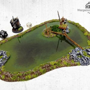 May include: A miniature wargaming terrain piece depicting a pond with a bridge, rocks, and vegetation. Includes a miniature figure, dice, and the HRC Wargaming Terrain logo. The pond is a dark green color.