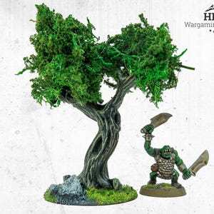 May include: A miniature wargaming terrain set. It features a detailed tree with green foliage and a miniature orc figure holding two blades. The tree has a textured, dark grey trunk and sits on a base with green moss.