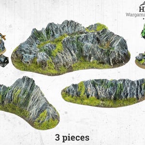 Könnte beinhalten: Dreiteiliges Wargaming-Geländeset mit felsigen Bergformationen mit grünen Moosakzenten. Enthält Miniaturfiguren und einen Würfel. Der Text "3 pieces" ist sichtbar. Das HRC Wargaming Terrain Logo ist oben rechts.