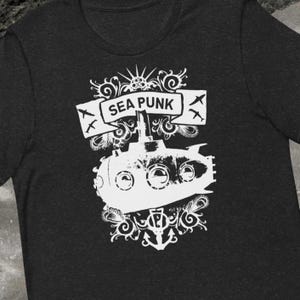 May include: Dark gray t-shirt featuring a white graphic of a submarine with the text "SEA PUNK" on a banner. The design includes decorative flourishes and an anchor.
