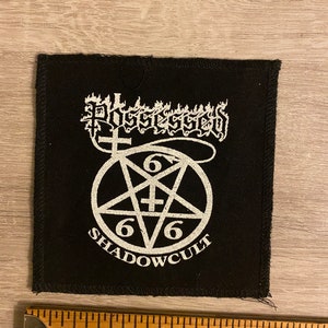 May include: Black square patch with white text and a pentagram design. The patch reads "Possessed" above a pentagram with the numbers "666" and the words "Shadowcult" below. A ruler is at the bottom.