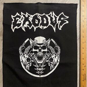 May include: Black square patch with the word "EXODUS" in white, jagged lettering above a white skull and horns design. The patch is approximately 8 inches by 8 inches.