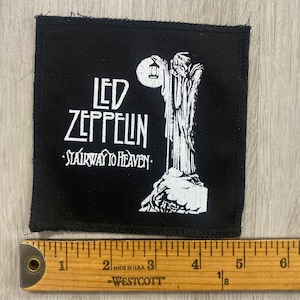 May include: Black square patch featuring the Led Zeppelin logo and the words "Stairway to Heaven" in white. The patch includes a white illustration of a figure holding a lantern. The patch measures approximately 3 inches by 3 inches.