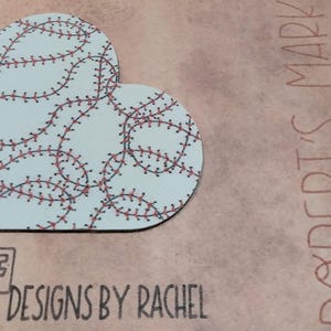 May include: A heart-shaped design with a baseball stitch pattern in red and black on a light blue background. The text "ROBERT'S MARK 1:3" is written in red. The logo "DESIGNS BY RACHEL" is at the bottom.