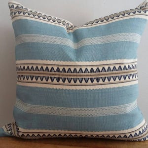 Puede incluir: Una almohada azul y blanca a rayas con un patr&oacute;n geom&eacute;trico en marr&oacute;n y negro. La almohada est&aacute; hecha de una tela suave y tejida.