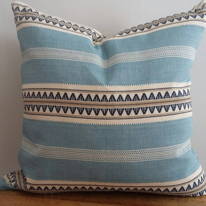 Puede incluir: Una almohada azul y blanca a rayas con un patr&oacute;n geom&eacute;trico en marr&oacute;n y negro. La almohada est&aacute; hecha de una tela suave y tejida.
