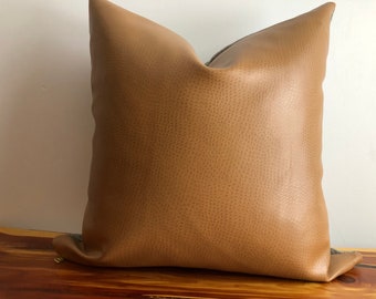 May include: A brown faux leather pillow with a subtle textured surface. The pillow has a zipper closure and a gray fabric lining.