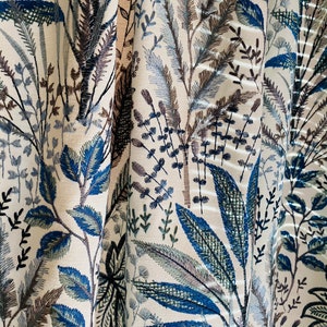 May include: Close-up of a cream-colored fabric with an embroidered floral pattern in shades of blue, green, and brown.