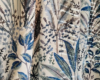 May include: Close-up of a cream-coloured fabric with an embroidered floral pattern in shades of blue, green, and brown.