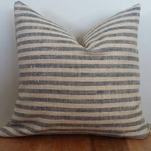 Puede incluir: Una almohada de rayas con fondo crema y rayas azul marino. La almohada est&aacute; hecha de una tela suave y texturizada.