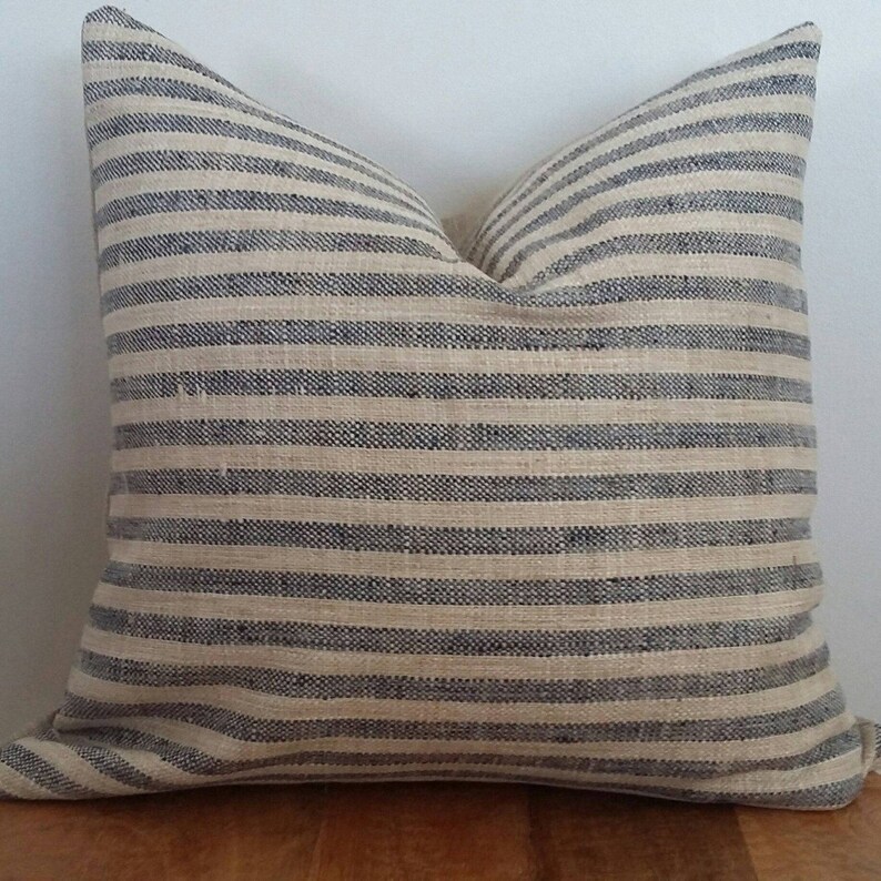 Puede incluir: Una almohada de rayas con fondo crema y rayas azul marino. La almohada est&aacute; hecha de una tela suave y texturizada.