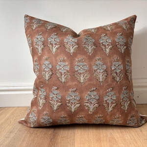 Puede incluir: Una almohada de tiro de color óxido con un patrón floral en tonos azules y marrones. La almohada está hecha de una tela suave y texturizada.