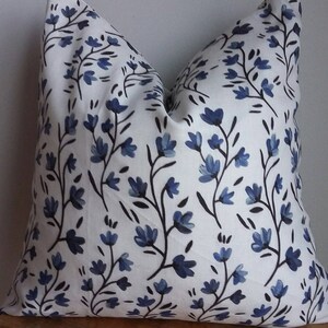 Puede incluir: Almohada blanca con un patr&oacute;n floral azul. Las flores son estilizadas y tienen un aspecto de acuarela. La almohada est&aacute; hecha de una tela suave y c&oacute;moda.