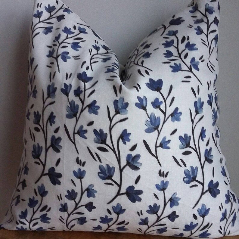 Puede incluir: Almohada blanca con un patr&oacute;n floral azul. Las flores son estilizadas y tienen un aspecto de acuarela. La almohada est&aacute; hecha de una tela suave y c&oacute;moda.