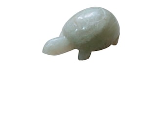May include: A small, light green turtle figurine carved from stone. The turtle has a rounded shell, a small head, and stubby legs. The stone has a slightly translucent quality.
