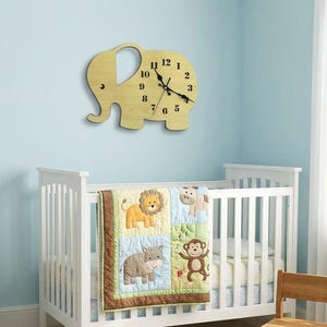 May include: A nursery scene with a white crib, a colorful animal-themed quilt, and a wooden elephant-shaped clock on a light blue wall. A small bookshelf with books and a teddy bear are also present.