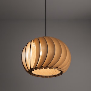 May include: A modern pendant light fixture with a spherical shade made of layered wooden slats. The light hangs from a black cord and ceiling mount. The warm wood tones and the light filtering through the slats create a soft glow.