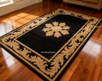 May include: A rectangular black area rug with a gold floral border and a central gold floral medallion. The rug is placed on a hardwood floor, and the design is traditional and elegant.