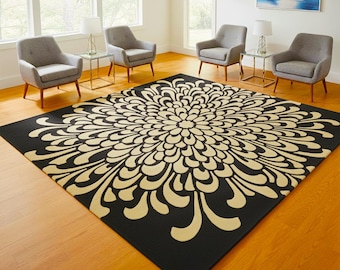 May include: A large, square black area rug with a cream-colored floral design. The rug is the focal point of a room with gray armchairs, glass-topped tables, and lamps. The room has hardwood floors and large windows.