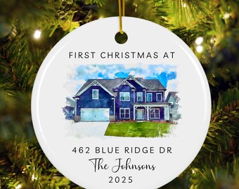 May include: A round white ceramic ornament featuring a watercolor illustration of a two-story blue house with a garage and green lawn. Text reads: FIRST CHRISTMAS AT, 462 BLUE RIDGE DR, The Johnsons, and 2025. A gold string is attached at the top.