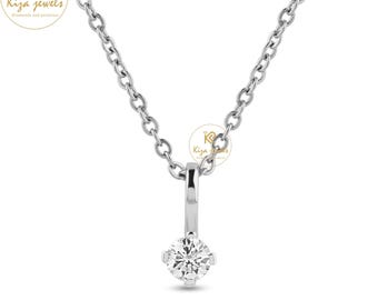 Puede incluir: Un delicado collar de plata con un colgante de diamante único. El diamante de talla redonda está engastado en un engaste de cuatro garras y cuelga de una fina cadena. El diseño es simple y elegante, destacando el brillo del diamante. El logotipo de la marca "Kiza Jewels" es visible.