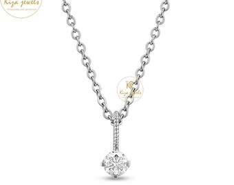 Puede incluir: Un collar de plata con un colgante de diamante claro y redondo. El colgante cuelga de una cadena fina. El collar se muestra sobre un fondo blanco. El logotipo de la marca "Kiza jewels" es visible.