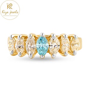 May include: A gold ring with a series of marquise-cut gemstones. The ring features a central light blue gemstone, with four light-coloured gemstones either side. The ring is from Kiza Jewels.