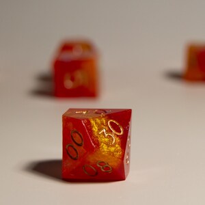 May include: A set of polyhedral dice with a red and gold color scheme. The dice are made of a translucent material, with gold-colored numbers. The dice are designed for tabletop role-playing games.