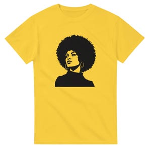 May include: A bright yellow short-sleeved t-shirt featuring a black graphic print on the chest. The graphic depicts a stylized silhouette of a person with a large afro hairstyle, wearing hoop earrings and a high-neck top, looking to the side.