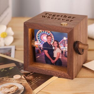 Op de afbeelding: Een houten fotoblok met een foto van een stel voor een reuzenrad. De tekst "Together Wherever" staat op de bovenkant. Er zit een kleine houten knop aan de zijkant. Het blok staat op een houten oppervlak.