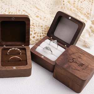 Könnte beinhalten: Drei Holzringboxen, zwei offen und eine geschlossen, mit Verlobungsringen. Die offenen Boxen zeigen Ringe auf einem Samtinnenraum. Die geschlossene Box hat den eingravierten Text: "OWEN & LUNA The Smith October 25, 2025."