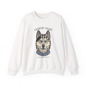 Puede incluir: Una sudadera blanca de manga larga con un gráfico central de una cabeza de husky diseñada con un patchwork de cuadros vichy en blanco y negro, patrones florales y texturas de mezclilla. El texto dice COUNTRY HEART y PATCHWORK HUSKY.