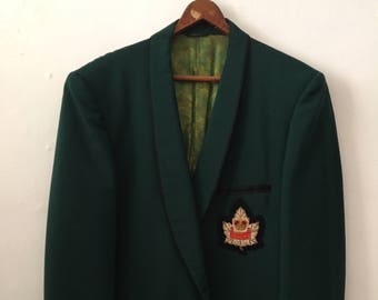 May include: A dark green blazer with a black velvet collar and a gold embroidered maple leaf with a crown on the right pocket.