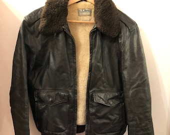 May include: A brown leather bomber jacket with a shearling collar and zipper closure. The jacket has two flap pockets on the front and a L.L.Bean label on the left chest.