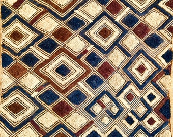 May include: A square woven rug with a geometric pattern in shades of brown, blue, and cream. The rug has a fringe border.