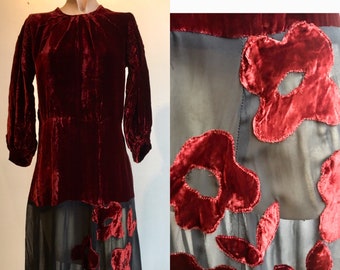May include: A vintage red velvet dress with a sheer black overlay and red velvet flower appliques. The dress has a round neckline and three-quarter sleeves.