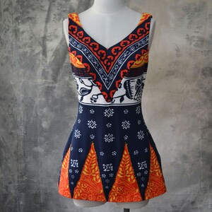 May include: A sleeveless, V-neck top on a mannequin. The top has a navy blue base with white, orange, and yellow geometric and floral patterns. The top has a fitted bodice and a flared hemline, showcasing a vintage style.