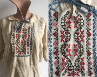 May include: A cream-colored embroidered blouse with a Peter Pan collar and long sleeves. The embroidery features a floral pattern in red, pink, green, and blue thread.