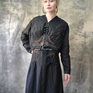 May include: A black long-sleeved dress with a decorative embroidered design on the bodice. The dress has a V-neckline and a belt.