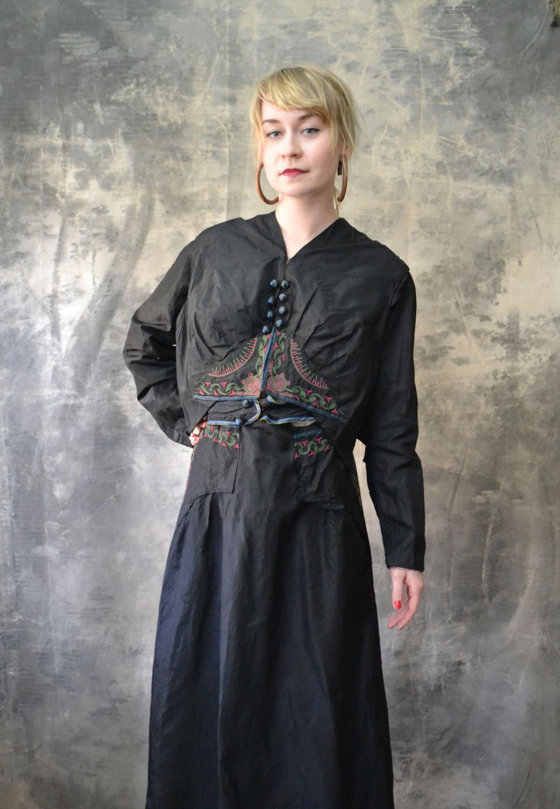 May include: A black long-sleeved dress with a decorative embroidered design on the bodice. The dress has a V-neckline and a belt.