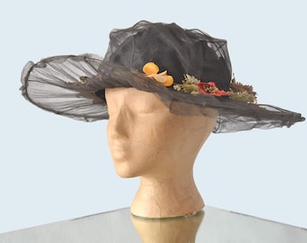 May include: A black wide-brimmed hat made of mesh with floral embellishments. The hat is sitting on a mannequin head.